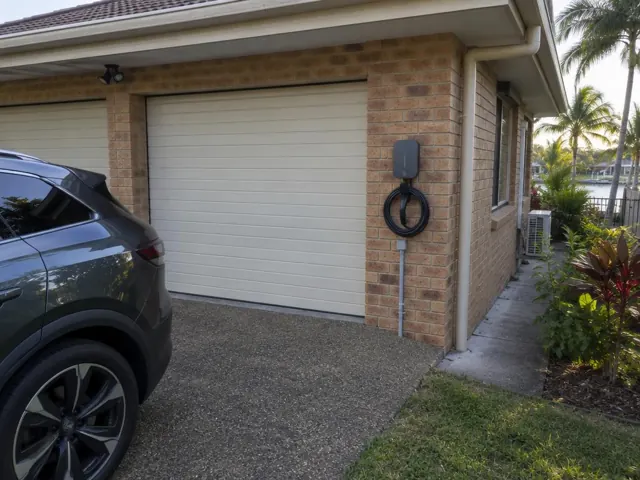 EV charger mounted on a brick garage wall beside a driveway and roller door in Paradise Point