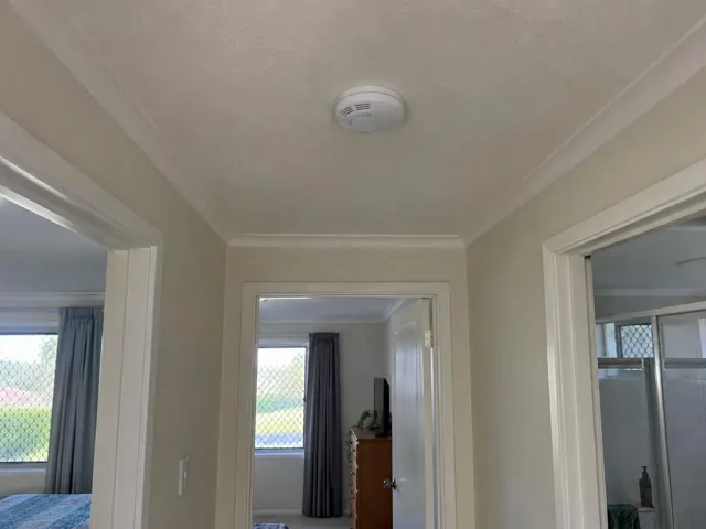 Ceiling smoke alarm in a hallway with white trim and beige walls in Runaway Bay
